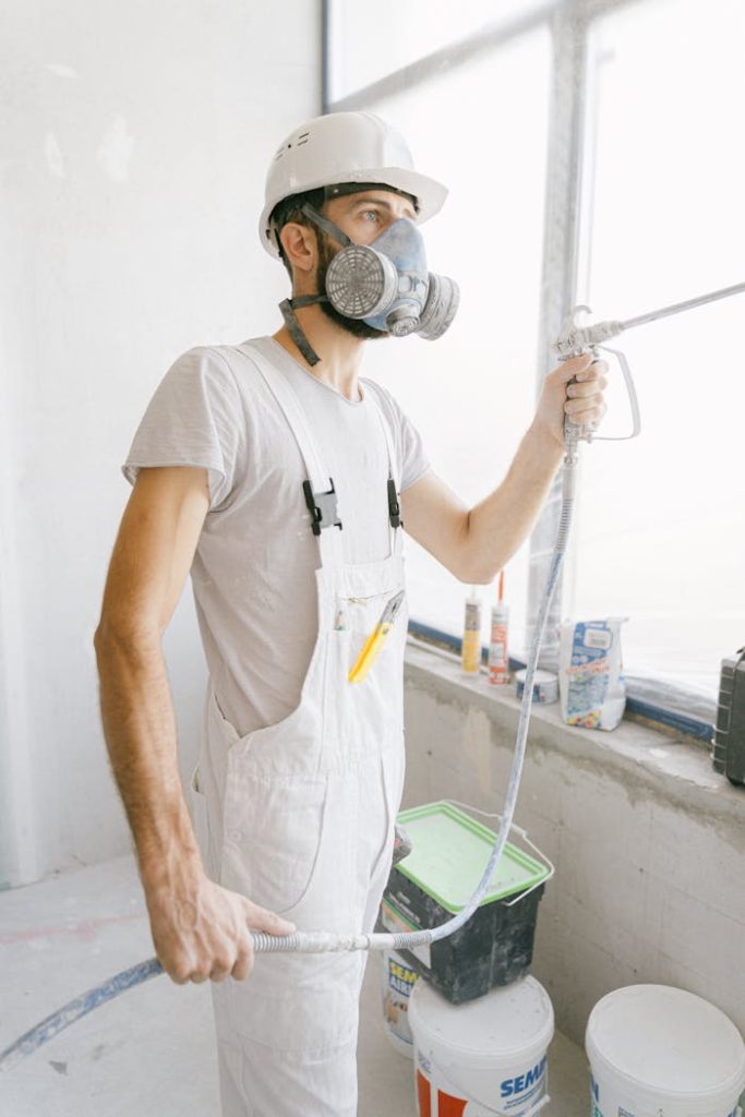 construction-worker-holding-a-hose-while-working-inside-a-house-5493668 Construction worker wearing safety gear and painting indoors.